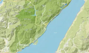 Il lungolago di Gardone Riviera si estende lungo il Lago di Garda, con montagne verdi che si affacciano sull'acqua.