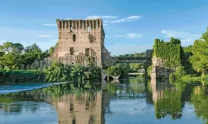Rovine di un castello e un ponte sul Mincio, con riflessi sull'acqua calma.