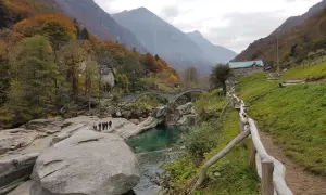 Sentiero sul monte Valdo, con un ponte ad arco in pietra, un fiume turchese e montagne sullo sfondo.