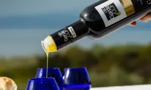 Versando olio Garda DOP in bicchierini blu, con pane fresco sullo sfondo.
