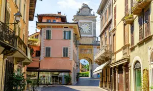 Un vicolo nel salò centro storico, con palazzi color pastello e un arco con orologio che conduce verso il lago.