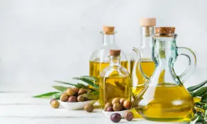 Bottiglie di vetro piene di olio extravergine di oliva dorato, con olive fresche e foglie di ulivo.