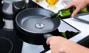Mani versano olio extravergine in una padella su un piano cottura a induzione. Si può friggere con olio extravergine per un gusto autentico.