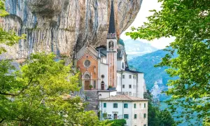 Suggestiva chiesa incastonata nella roccia, un gioiello architettonico vicino al Lago di Garda, circondata da verde lussureggiante e montagne.