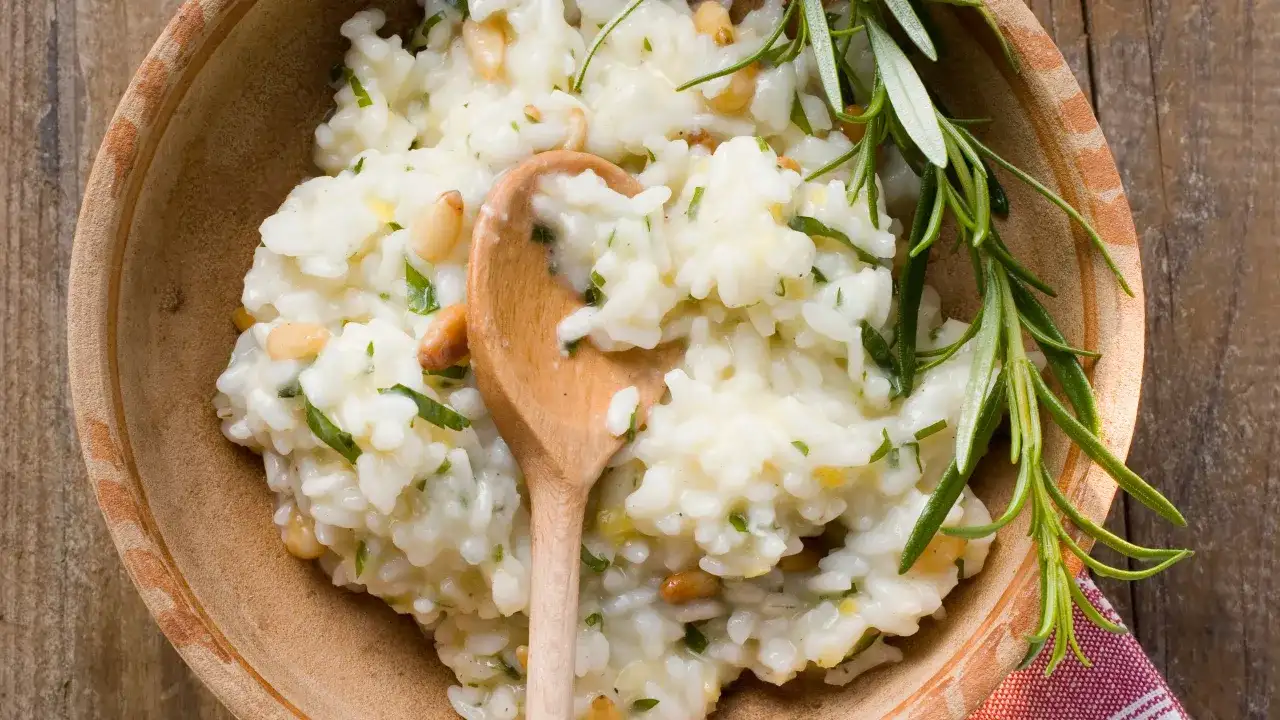 Un cremoso risotto al limone, guarnito con pinoli e rosmarino, servito in una ciotola di terracotta.