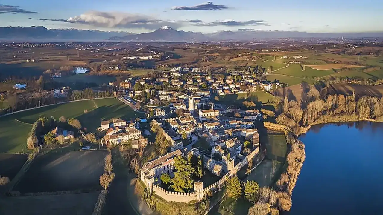 Vista aerea del borgo medievale di Castellaro Lagusello, con il castello fortificato, le case in pietra e il lago azzurro.