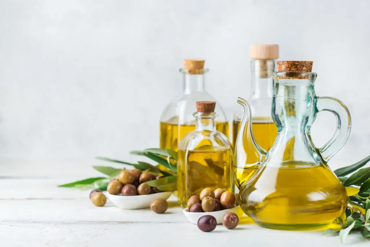 Bottiglie di vetro piene di olio extravergine di oliva dorato, con olive fresche e foglie di ulivo.