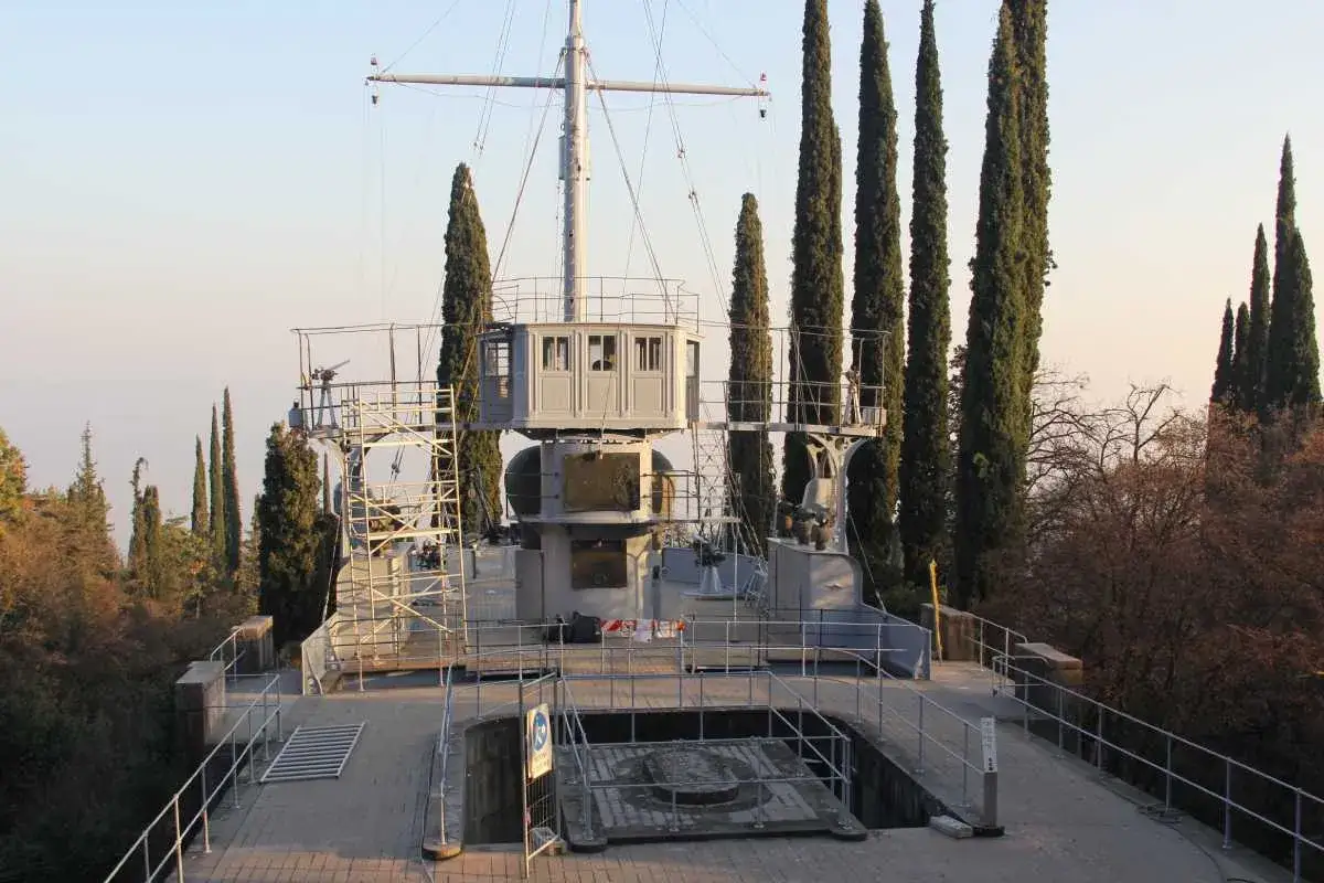La prua di una nave da guerra, parte del Vittoriale degli Italiani, si erge tra alti cipressi.
