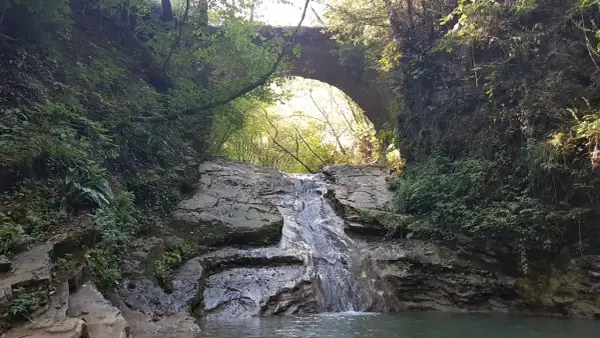 Cascate Torri del Benaco: un sentiero nascosto tra rocce e vegetazione lussureggiante, con un antico ponte ad arco che sovrasta la cascata.
