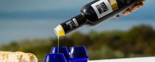 Versando olio Garda DOP in bicchierini blu, con pane fresco sullo sfondo.