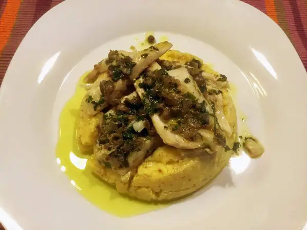 Delizioso luccio alla gardesana su un letto di polenta, condito con erbe aromatiche e olio d'oliva.
