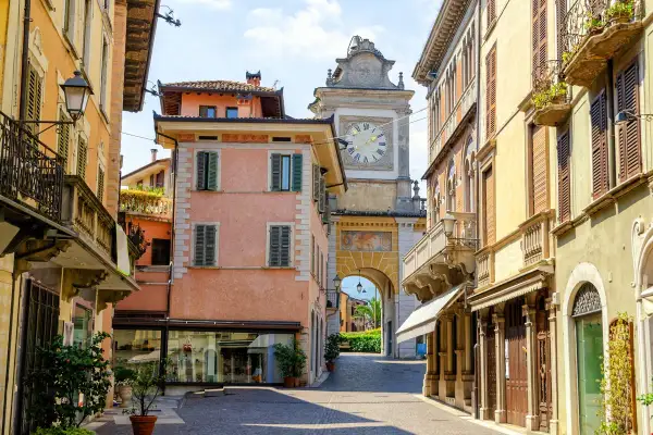 Un vicolo nel salò centro storico, con palazzi color pastello e un arco con orologio che conduce verso il lago.