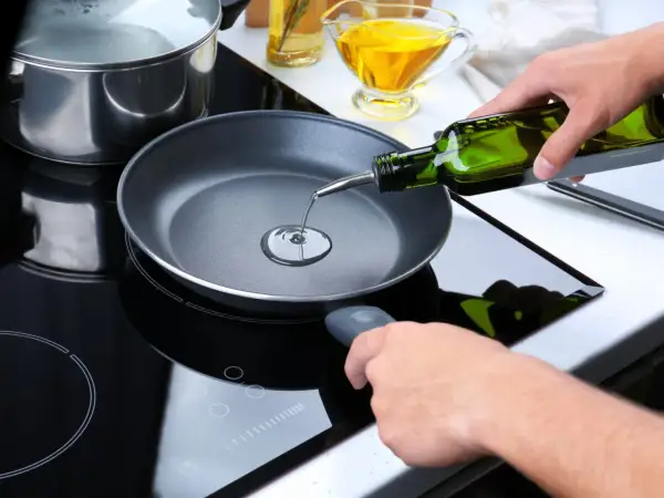 Mani versano olio extravergine in una padella su un piano cottura a induzione. Si può friggere con olio extravergine per un gusto autentico.