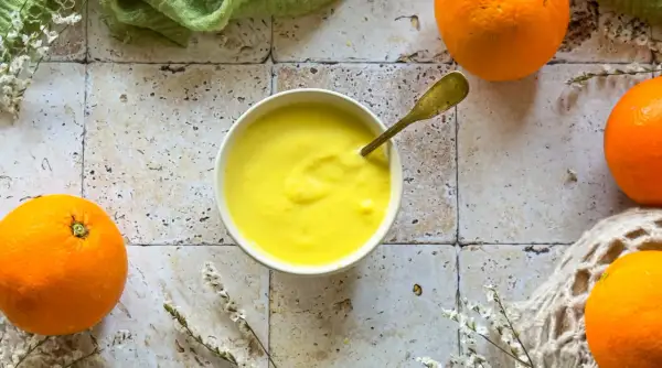 Crema gialla e liscia in una ciotola, con arance fresche intorno. Un cucchiaio dorato è immerso nella crema, che ricorda il sapore del sale all'arancia.