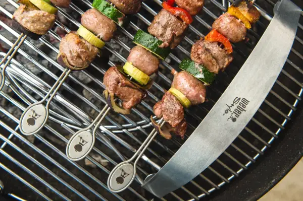 Spiedo di carne mista succulenta e verdure grigliate su una griglia Weber.